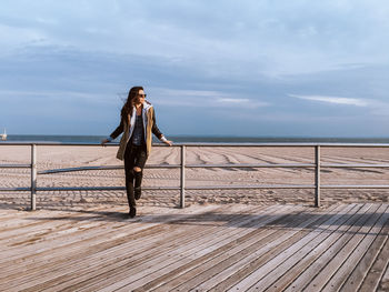 Woman standing on railing by sea against sky