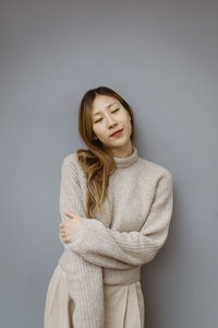 Young woman with eyes closed standing against gray background