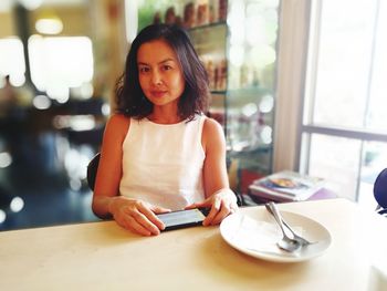 Portrait of woman sitting with mobile phone at restaurant