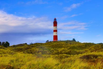 Lighthouse on field by building against sky