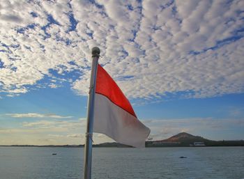 Red flag on pole by sea against sky