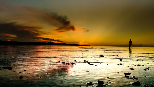 Silhouette person standing on sea against sky during sunset