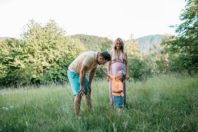 Family standing on grassy field against clear sky