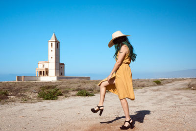 A young girl posing in a hat in the desert with a church in the background. lifestyle concept