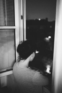 Rear view of thoughtful woman standing with arms crossed by window at night