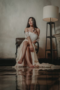 Woman sitting on chair against wall at home