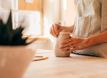 Midsection of woman molding a shape on table