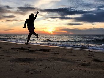 Silhouette woman on beach against sky during sunset