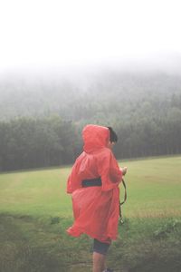 Person wearing raincoat on field against sky