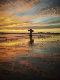 Man standing on beach against cloudy sky during sunset