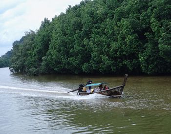 People on boat in river against trees