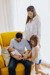 Father with newborn son in yellow armchair. family of four. dad son mom and daughter