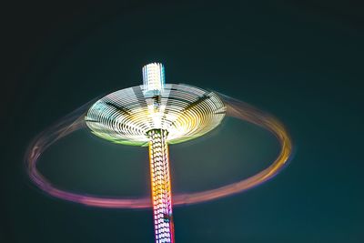 Low angle view of illuminated chain swing ride against clear sky at night