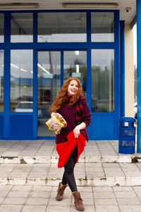 A cheerful red-haired young woman comes out of the store with bread