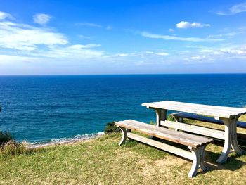 Bench by sea against blue sky