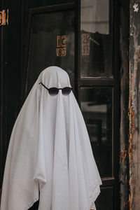 Person covering face with blanket while holding sunglasses standing outdoors