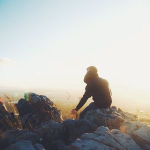 Man standing on rock against sky during sunset