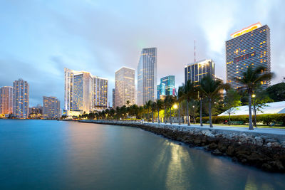 Modern cityscape by river against sky in city