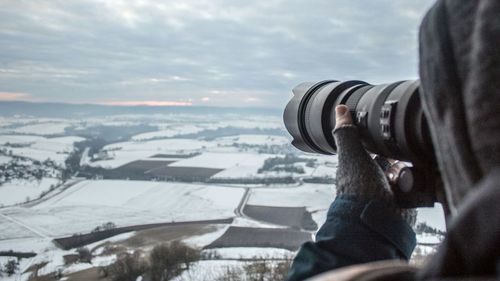 Close-up of man with camera against sky during winter