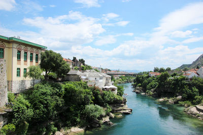 View of buildings by river against cloudy sky