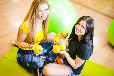 Portrait of smiling young friends holding apples while sitting at yoga studio