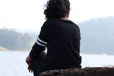 Rear view of woman sitting on rock against sky