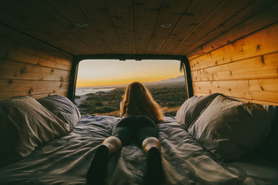 Young woman looking out to ocean from bed of camper van in mexico.