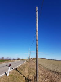 Road amidst field against clear blue sky