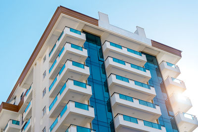 Corner of a residential apartment building with balconies against the blue sky.