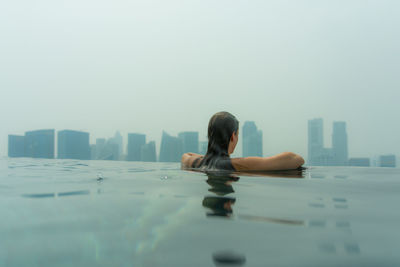 Rear view of woman in infinity pool against skyscrapers