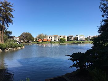 Scenic view of river by buildings against clear blue sky