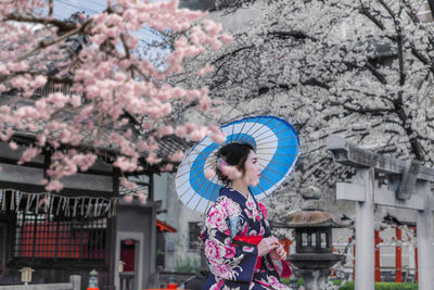 Asian woman wearing japanese traditional kimono sitting among the cherry blossoms in spring