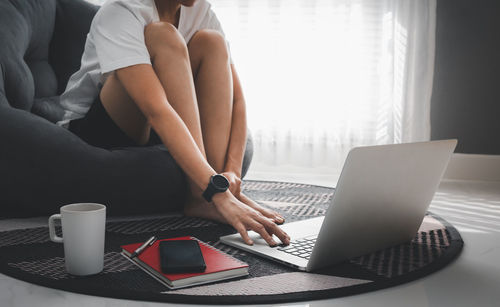 Low section of woman using laptop on carpet at home