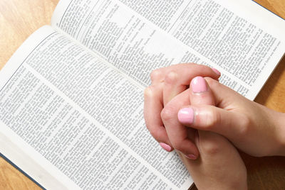 Close-up of woman with clasped hands reading bible