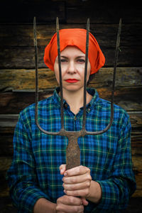 Beautiful woman holding gardening equipment while standing against wooden wall