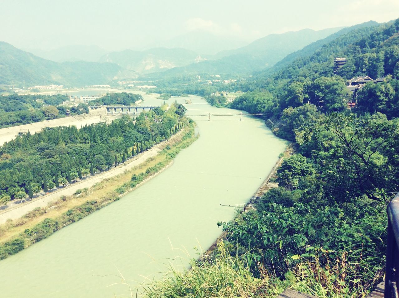 mountain, tree, high angle view, water, landscape, scenics, mountain range, built structure, tranquility, tranquil scene, architecture, river, nature, beauty in nature, building exterior, sky, green color, growth, road, hill