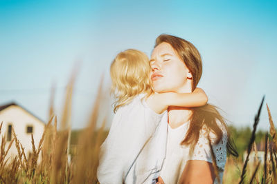 Young woman mom with baby girl on hands hug in backyard of cottage in sunset light