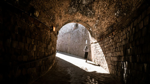 Rear view of woman walking on archway during sunny day