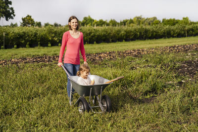 Smiling mother with daughter sitting in wheelbarrow