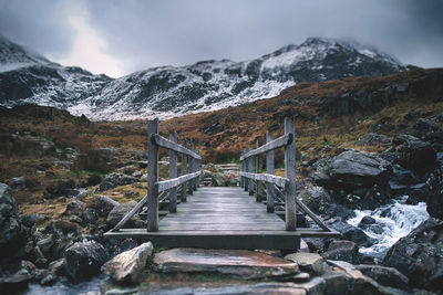 Footbridge over lake against mountains during winter