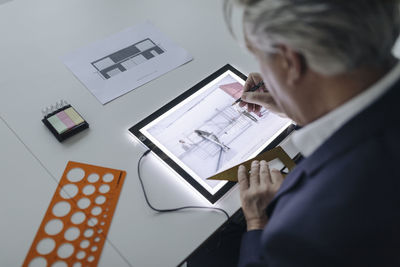 Senior businessman drawing on shining tablet