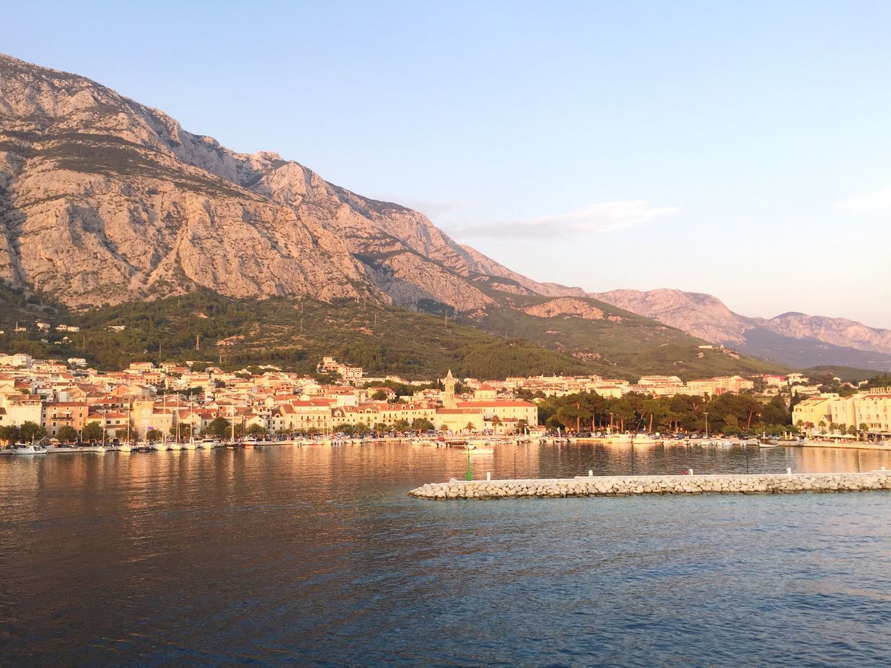 mountain, water, waterfront, built structure, architecture, mountain range, lake, river, tranquil scene, tranquility, scenics, town, nature, beauty in nature, sky, outdoors, rippled, day, no people, hill, idyllic, residential district, landscape, blue, non-urban scene