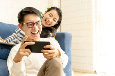 Woman sitting by man using phone at home
