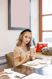 A pretty girl is sitting in a cozy christmas cafe with a cup of coffee in her hand and dreaming
