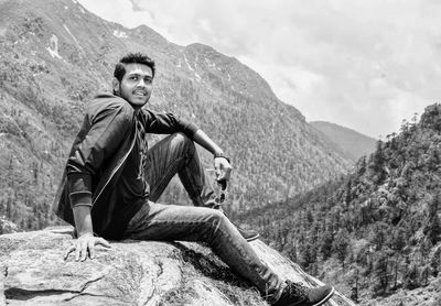 Portrait of young man sitting on rock against mountains