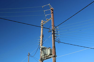 Low angle view of electricity pylon against clear blue sky