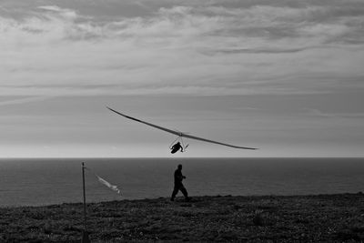 Side view of man walking by hang glider flying above sea