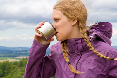 Close-up of woman drinking water from bottle cap against sky