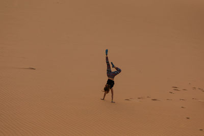 High angle view of teenager doing handstand on sand at beach