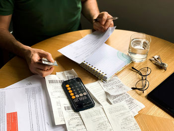 Man is making audit of household expenses using calculator and notebook. lots of receipts and bills